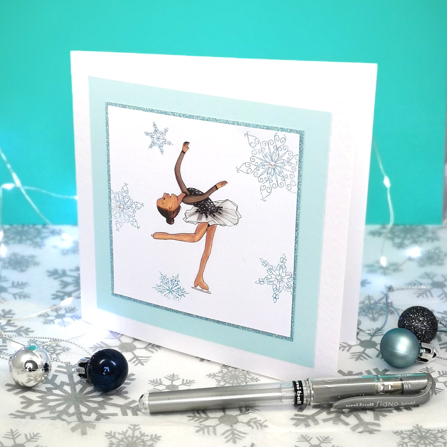 6 x 6 inch greeting card with image of a figure skater in a black dress, surrounded by blue foiled ornate snowflakes