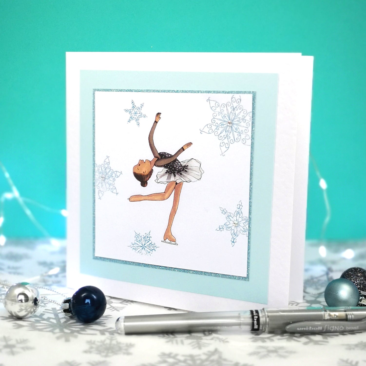 6 x 6 inch greeting card with image of a figure skater in a black dress, surrounded by blue foiled ornate snowflakes