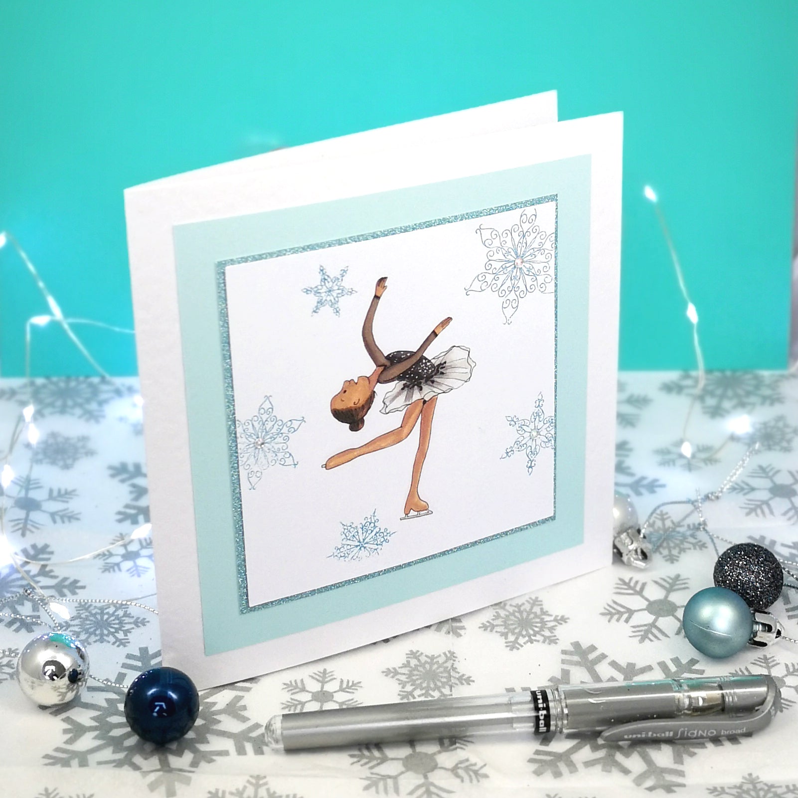 6 x 6 inch greeting card with image of a figure skater in a black dress, surrounded by blue foiled ornate snowflakes