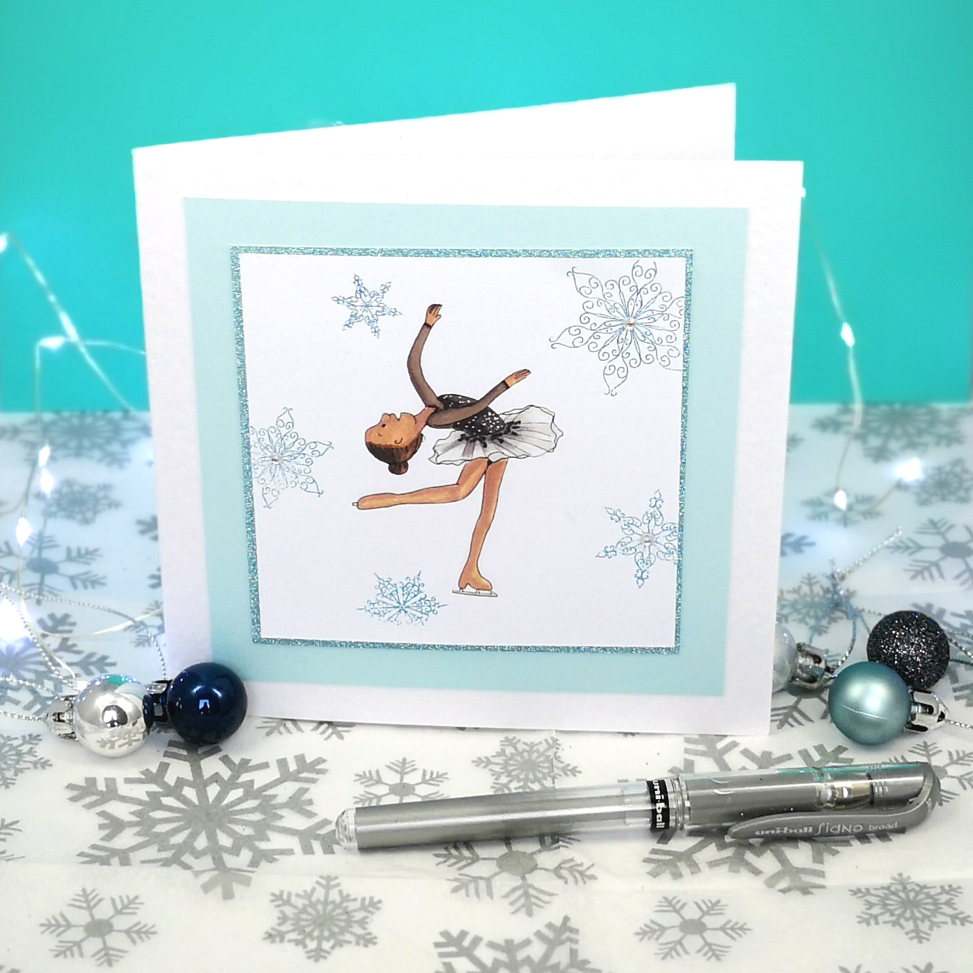 6 x 6 inch greeting card with image of a figure skater in a black dress, surrounded by blue foiled ornate snowflakes