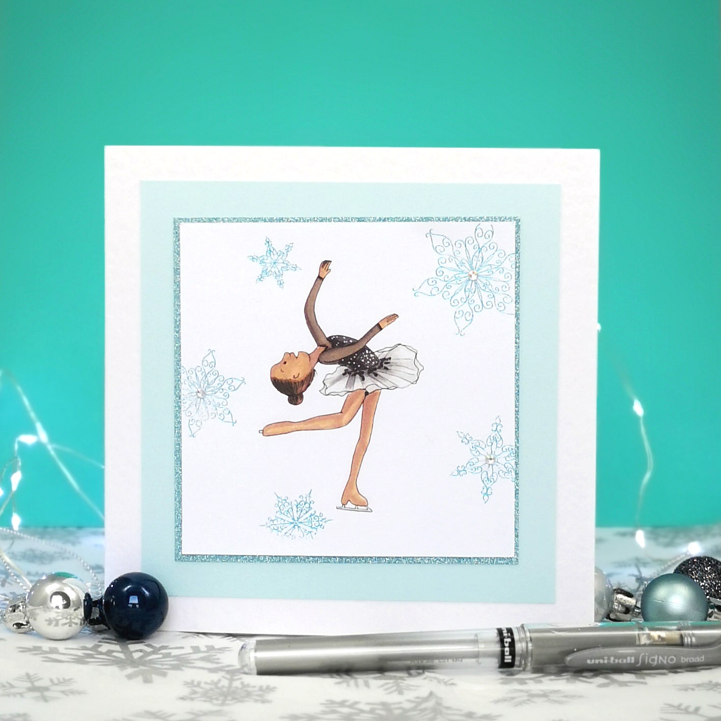 6 x 6 inch greeting card with image of a figure skater in a black dress, surrounded by blue foiled ornate snowflakes