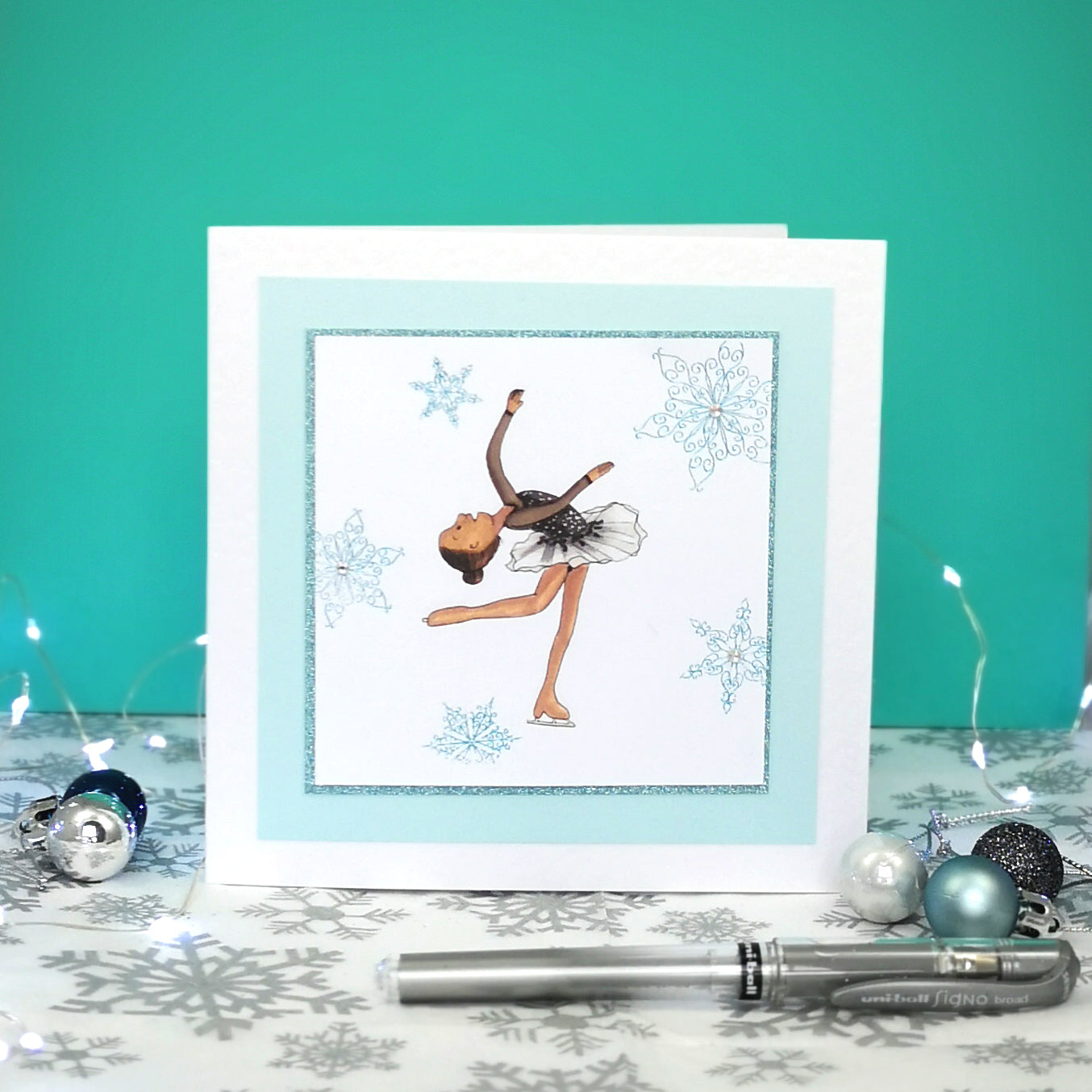 6 x 6 inch greeting card with image of a figure skater in a black dress, surrounded by blue foiled ornate snowflakes