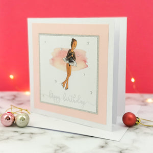 6 x 6 inch birthday card with image of a figure skater mid-flight, wearing a black dress. Pink watercolour brush stroke behind the figure skater illustration, with a silver foiled happy birthday script greeting and surrounded by clear/silver rhinestone gems