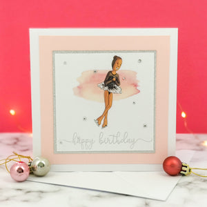 6 x 6 inch birthday card with image of a figure skater mid-flight, wearing a black dress. Pink watercolour brush stroke behind the figure skater illustration, with a silver foiled happy birthday script greeting and surrounded by clear/silver rhinestone gems