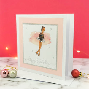 6 x 6 inch birthday card with image of a figure skater mid-flight, wearing a black dress. Pink watercolour brush stroke behind the figure skater illustration, with a silver foiled happy birthday script greeting and surrounded by clear/silver rhinestone gems