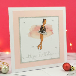 6 x 6 inch birthday card with image of a figure skater mid-flight, wearing a black dress. Pink watercolour brush stroke behind the figure skater illustration, with a silver foiled happy birthday script greeting and surrounded by clear/silver rhinestone gems